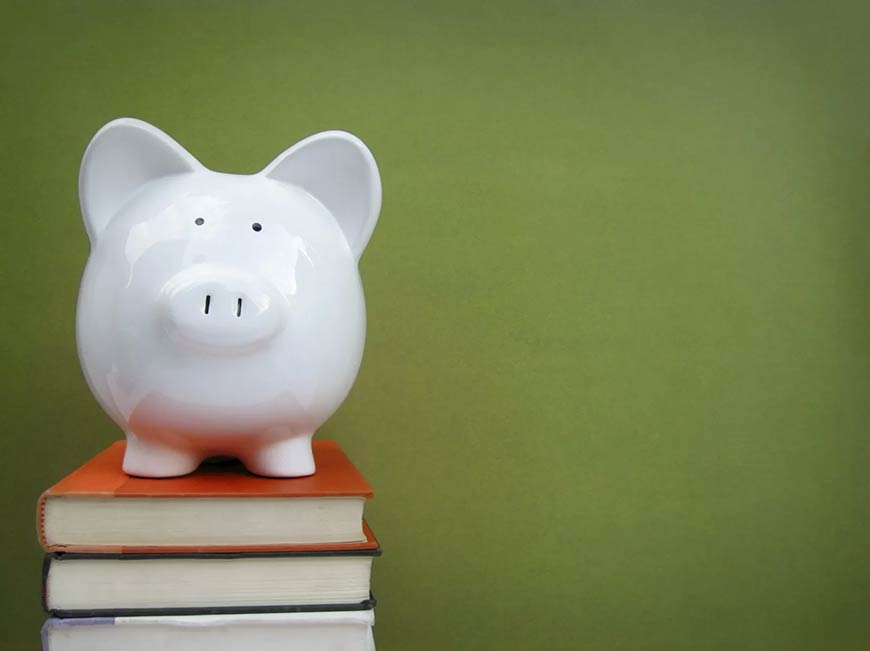 Photo of a piggy bank sitting on top of a stack of books on a green background